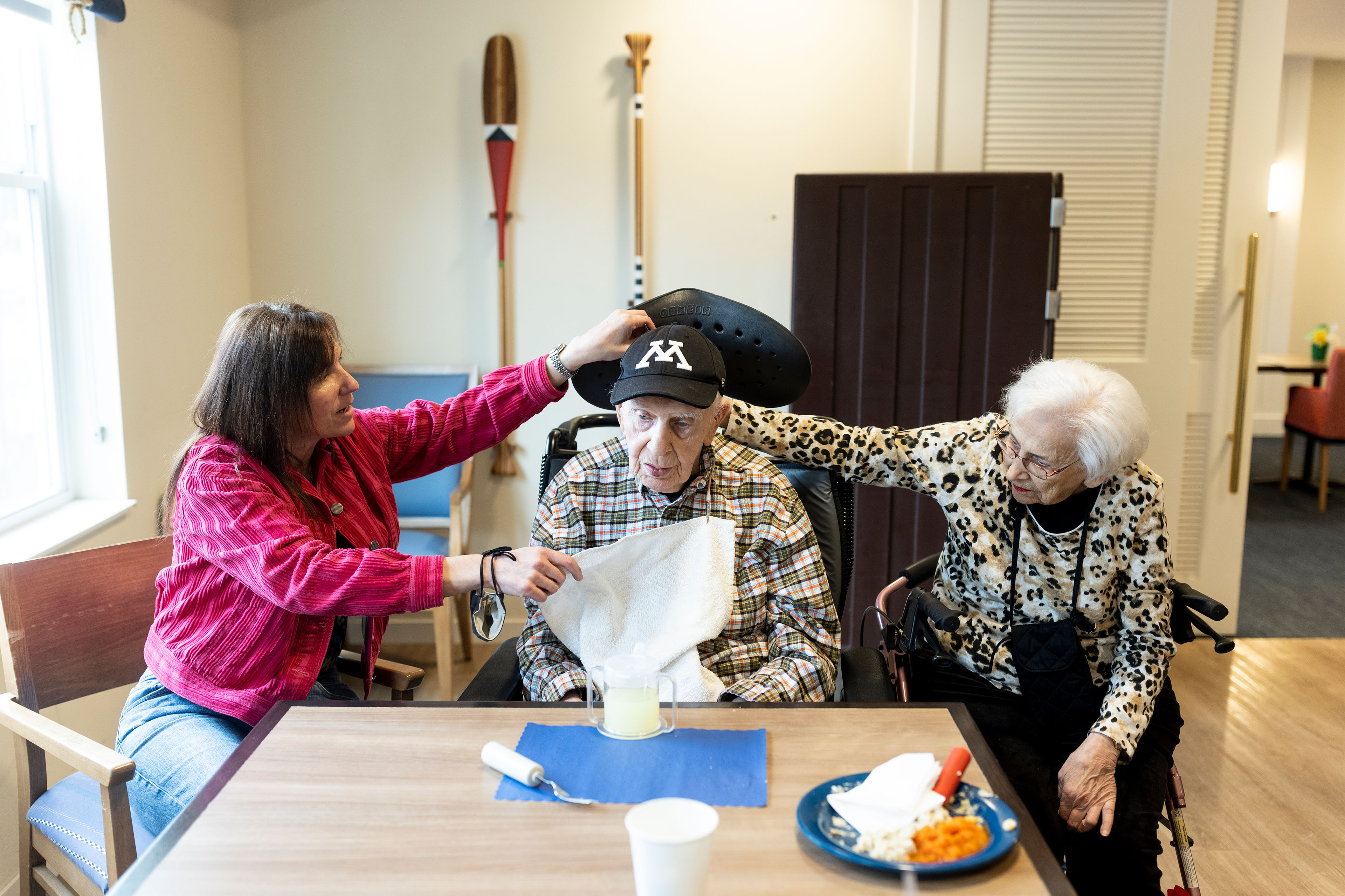 A photo of an elderly man being assisted by his wife and daughter while sitting at a table.