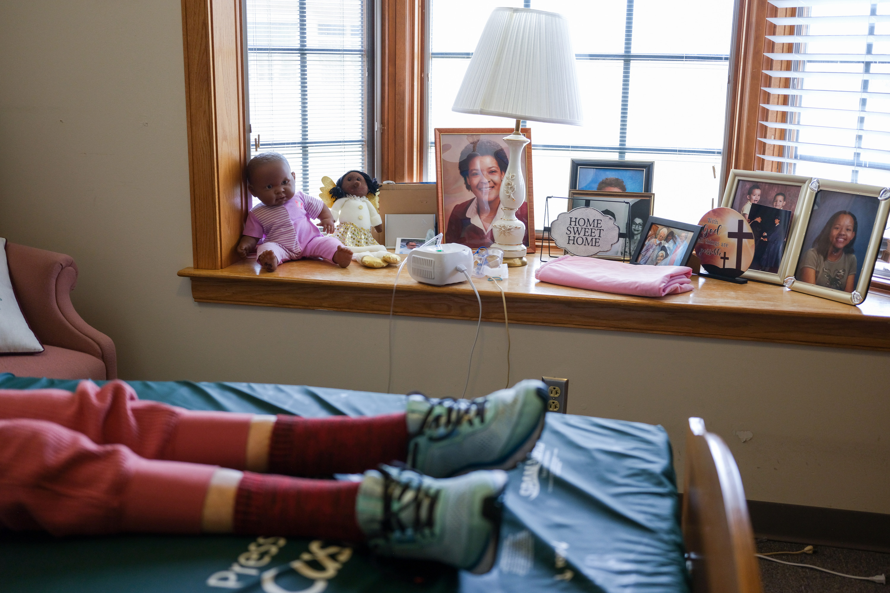 A photo of an elderly woman's legs lying in bed. Old photos rest on the windowsill next to her.