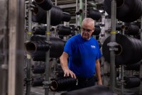 A man in a blue tshirt and glasses stands in a factory