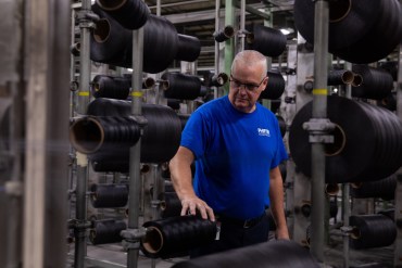 A man in a blue tshirt and glasses stands in a factory