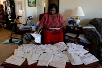 A woman in a red striped blouse and red skirt sits in an armchair in front coffee table, the surface of which is covered in mailing envelopes and papers.