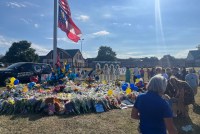 A photo of a flagpole surrounded by bouquets and stuffed animals outside of a school.