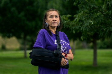 A woman with a protective sling on her arm stands outside to have her portrait taken.