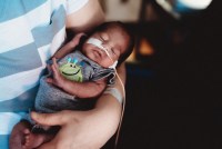 A premature newborn is cared for in the neonatal intensive care unit while being held in a person's arms.