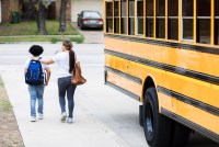 A photo of a boy walking home with his mother after being dropped off by the school bus.