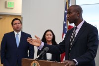 Florida Surgeon General Joe Ladapo speaks at a podium. Florida Gov. Ron Desantis stands beside him.