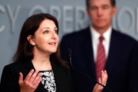 A photo of a woman talking at a press conference at a microphone.