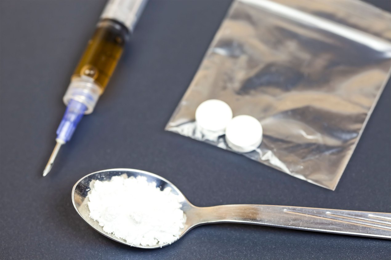 A stock photo of various illegal drugs: a syringe of heroin, fentanyl, and cocaine.