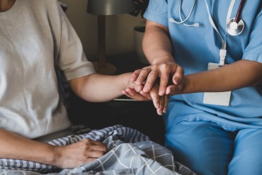 A nurse holds the hand of a patient in a home setting.