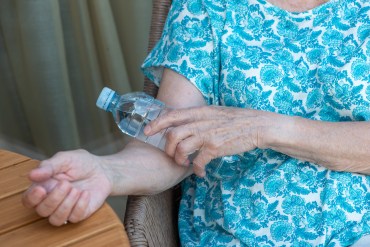 A photo of an elderly woman holding a cold water bottle to her forearm to cool herself down.