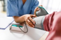 A close up photograph of an unrecognizable female nurse measuring blood pressure of a woman.