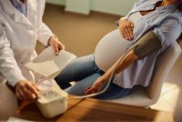 A photo of a pregnant woman having her blood pressure measured by a doctor.