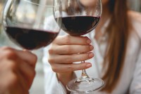 Two women toast their glasses of red wine.