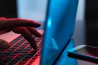 A photo shows a hand typing on a laptop, colored with blue and red light.