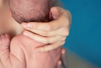 A photo shows a mother's hands holding a newborn baby.