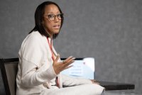 A photo of a Black woman sitting and speaking to someone out of frame.