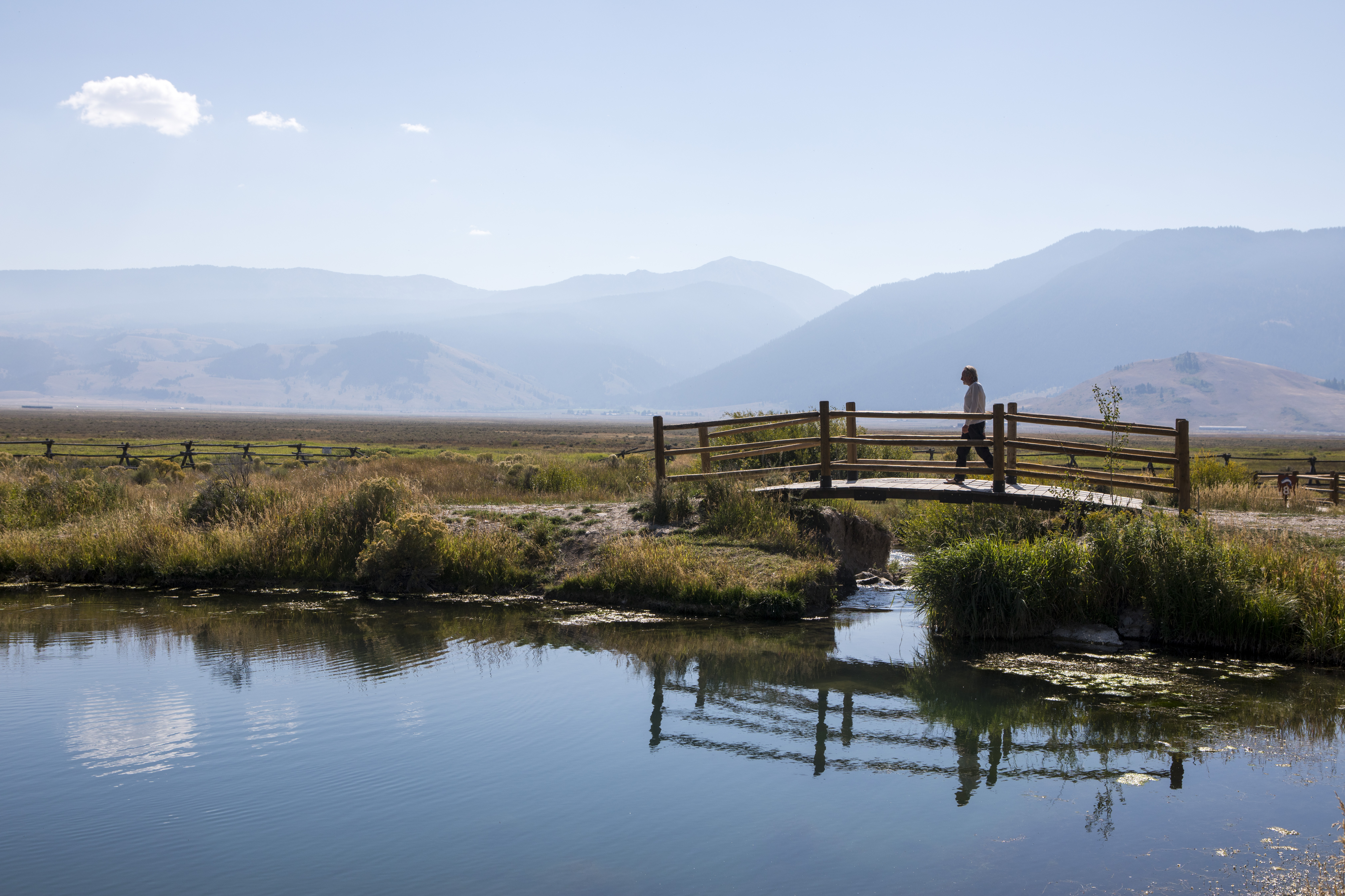 A man walks across a wooden bridge over a river 