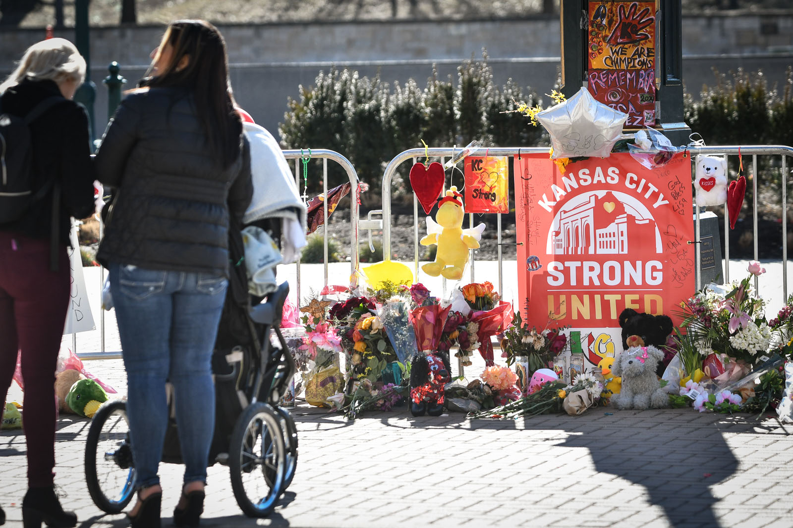 An outdoor memorial is sat up near Union Station in Kansas City. There is a sign that reads, "Kansas City / Strong / United." Flowers, stuffed animals, and other memorial gifts surround the sign.