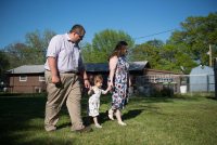 A photo of two parents walking with their young daughter outside.