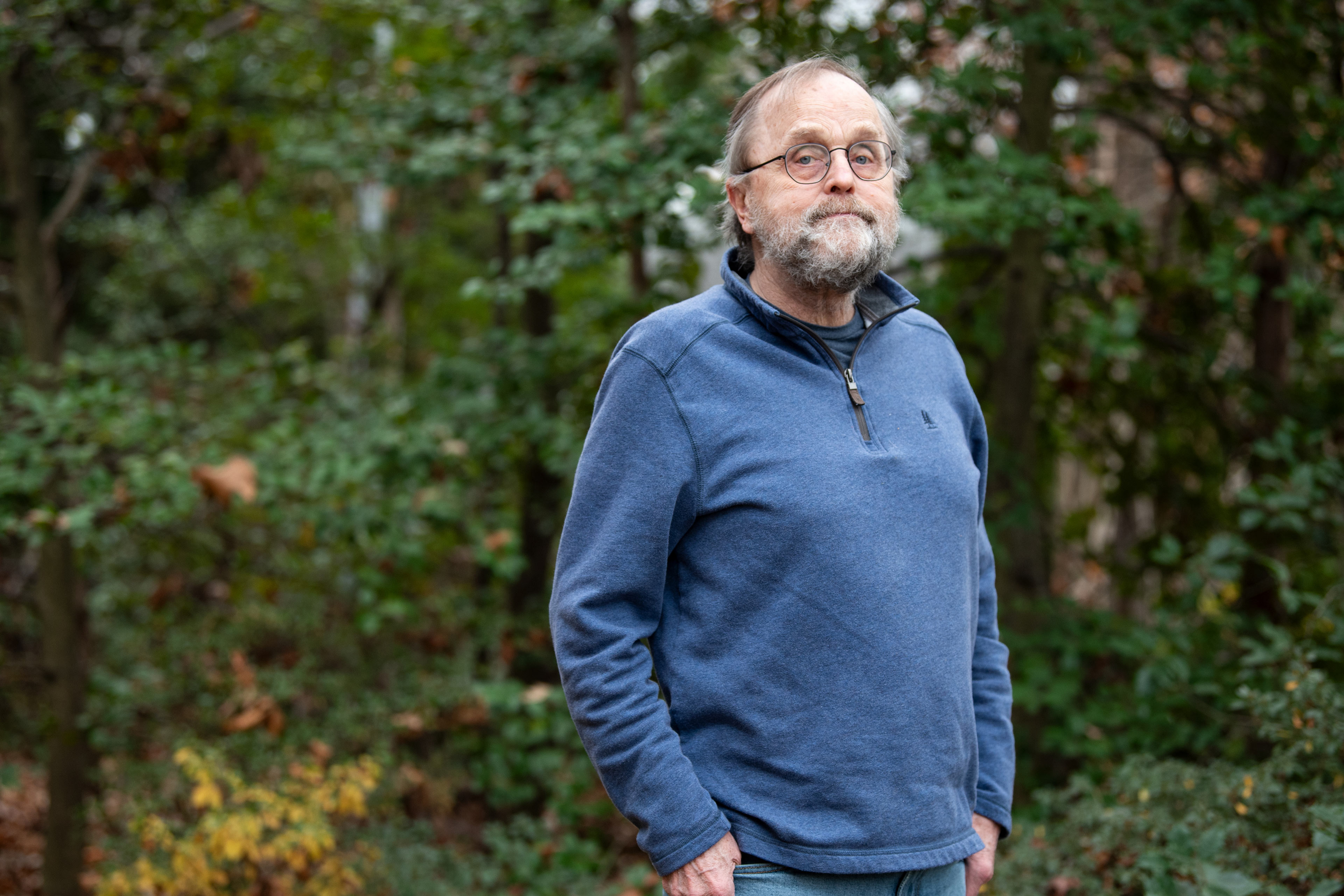 A portrait of a man standing outside with his hands in his pockets.