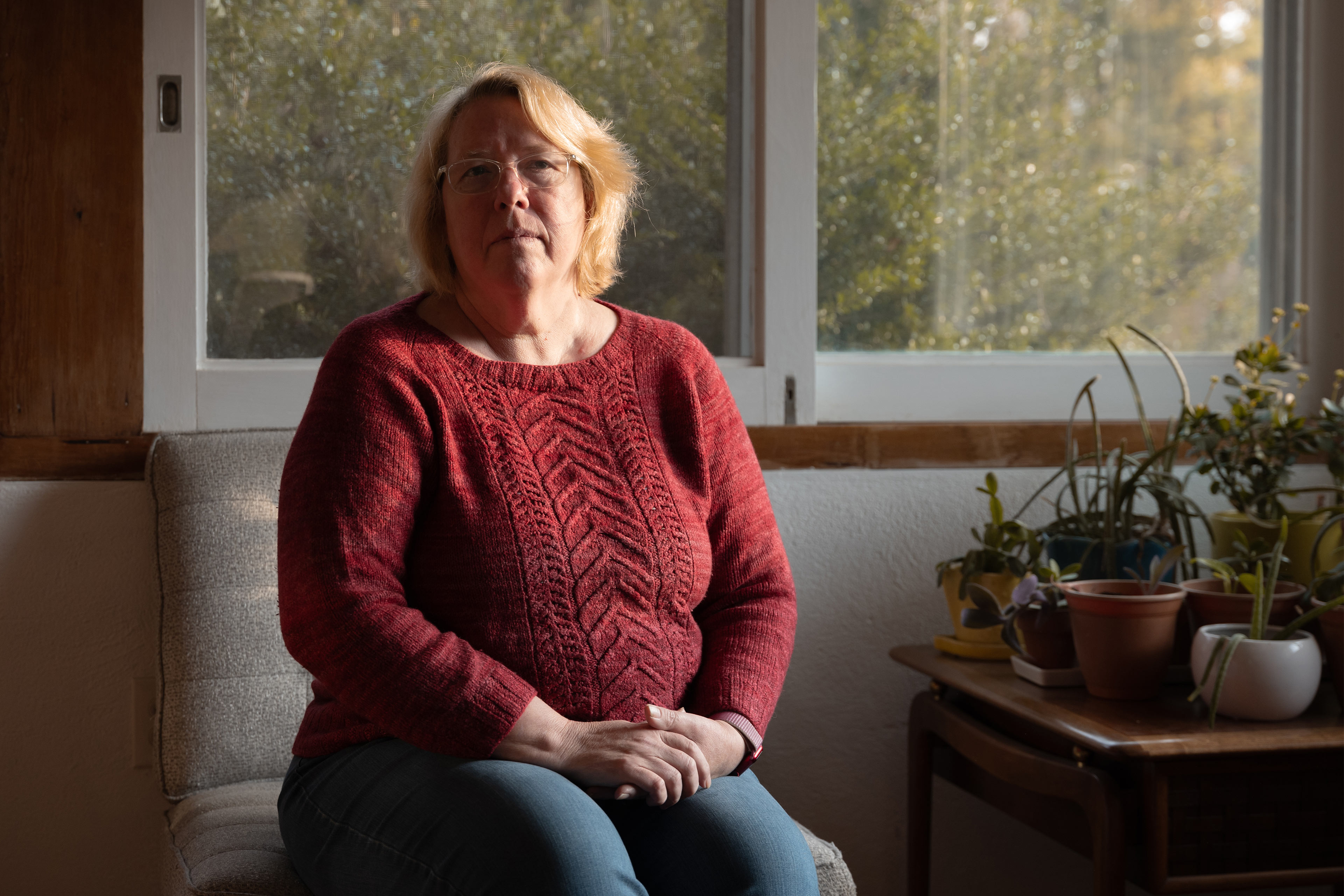 A portrait of a woman sitting indoors by a set of windows.