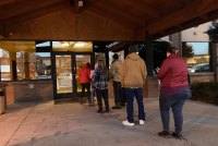 A line of six people are lined up outside the entrance doors of a building.